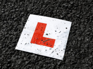 Learner drive red L plate against black tarmac