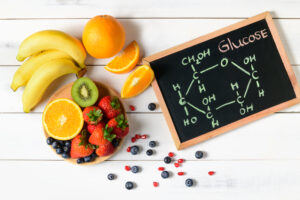 Glucose chemical molecules on blackboard with fresh fruit bowl